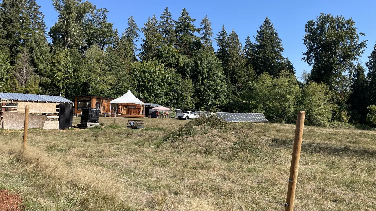 A small high-peak tent on a rural lot with a cabin, solar array, and treeline behind