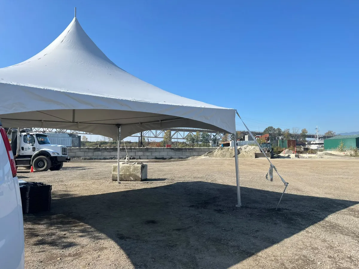 A single high-peak frame tent ballasted with a concrete block on a gravel lot by the river in New Westminster