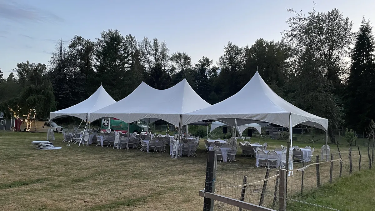 Three joined high-peak marquees on a Langley acreage at dusk, banquet tables and chairs underneath