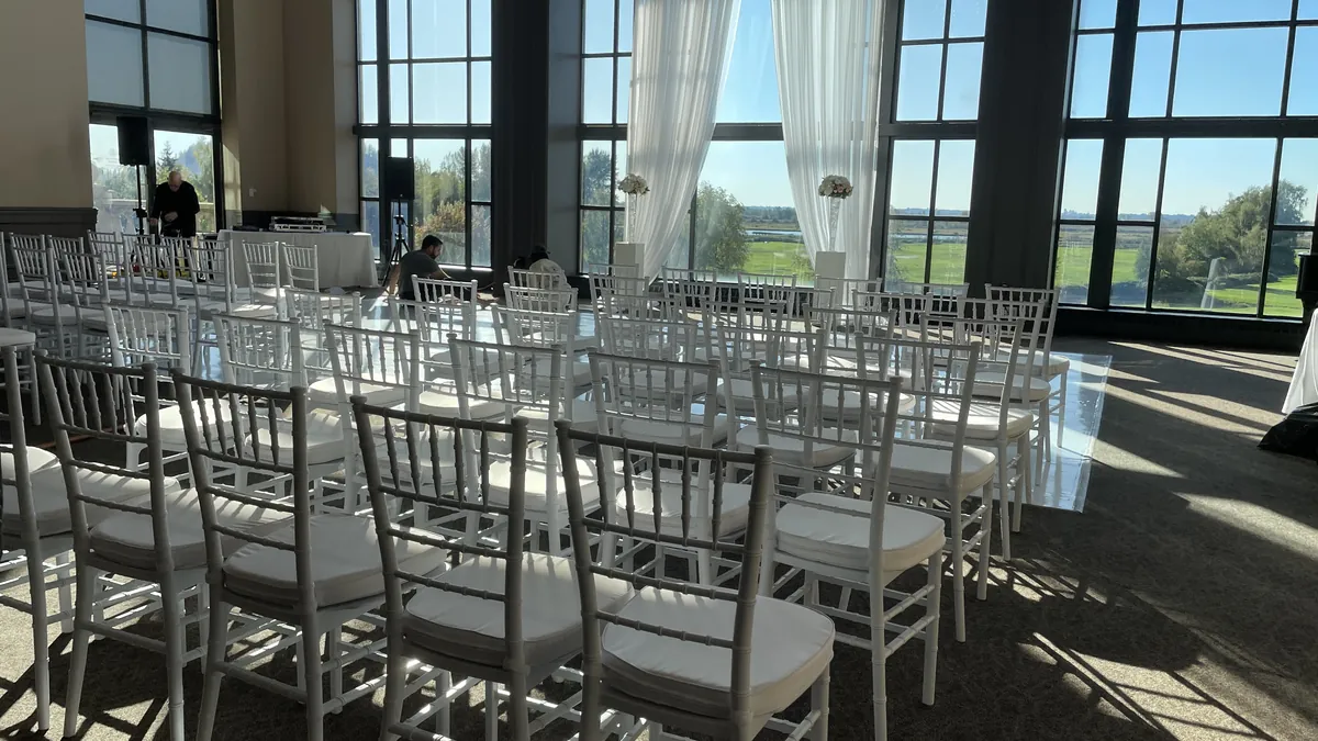 White Chiavari chairs in ceremony rows and a white dance floor in the Swaneset Bay ballroom, golf course visible through the windows