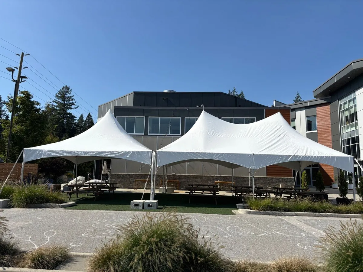 Twin white high-peak tents over picnic tables on an office patio, ballasted with concrete blocks