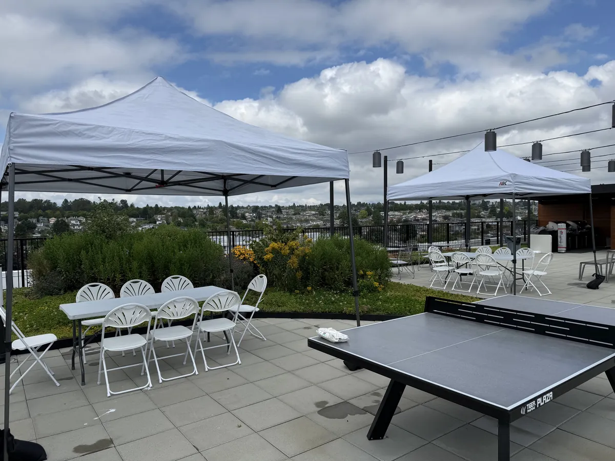 Two pop-up canopies, banquet tables, fanback chairs, and a ping-pong table on a rooftop patio
