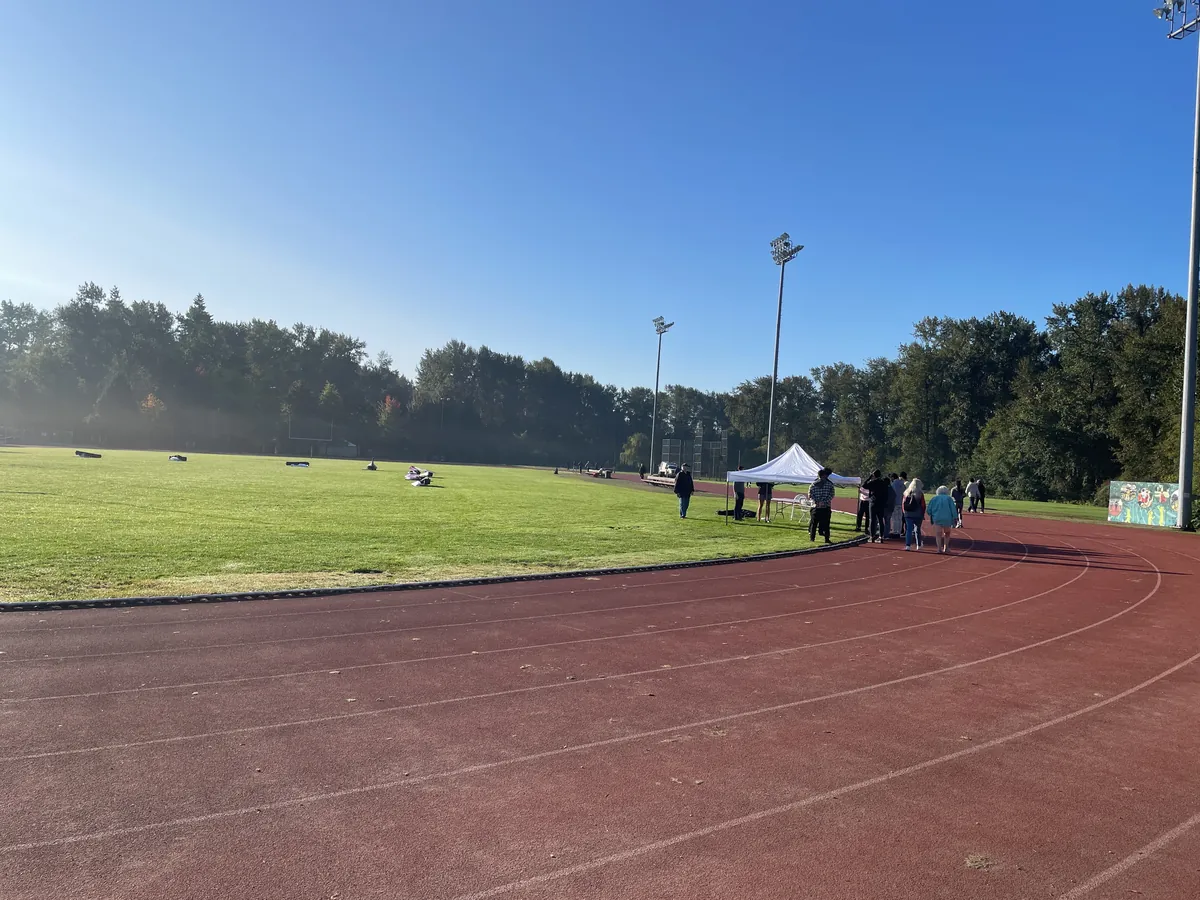 A white pop-up canopy and folding tables on a running track for a sports-day job