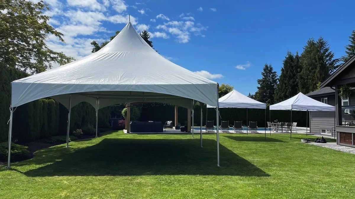 A large high-peak tent and two canopies set up in a backyard beside a pool