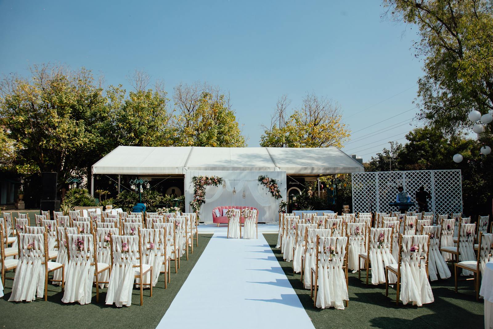 A row of wooden chairs draped in white fabric with floral accents on a green lawn