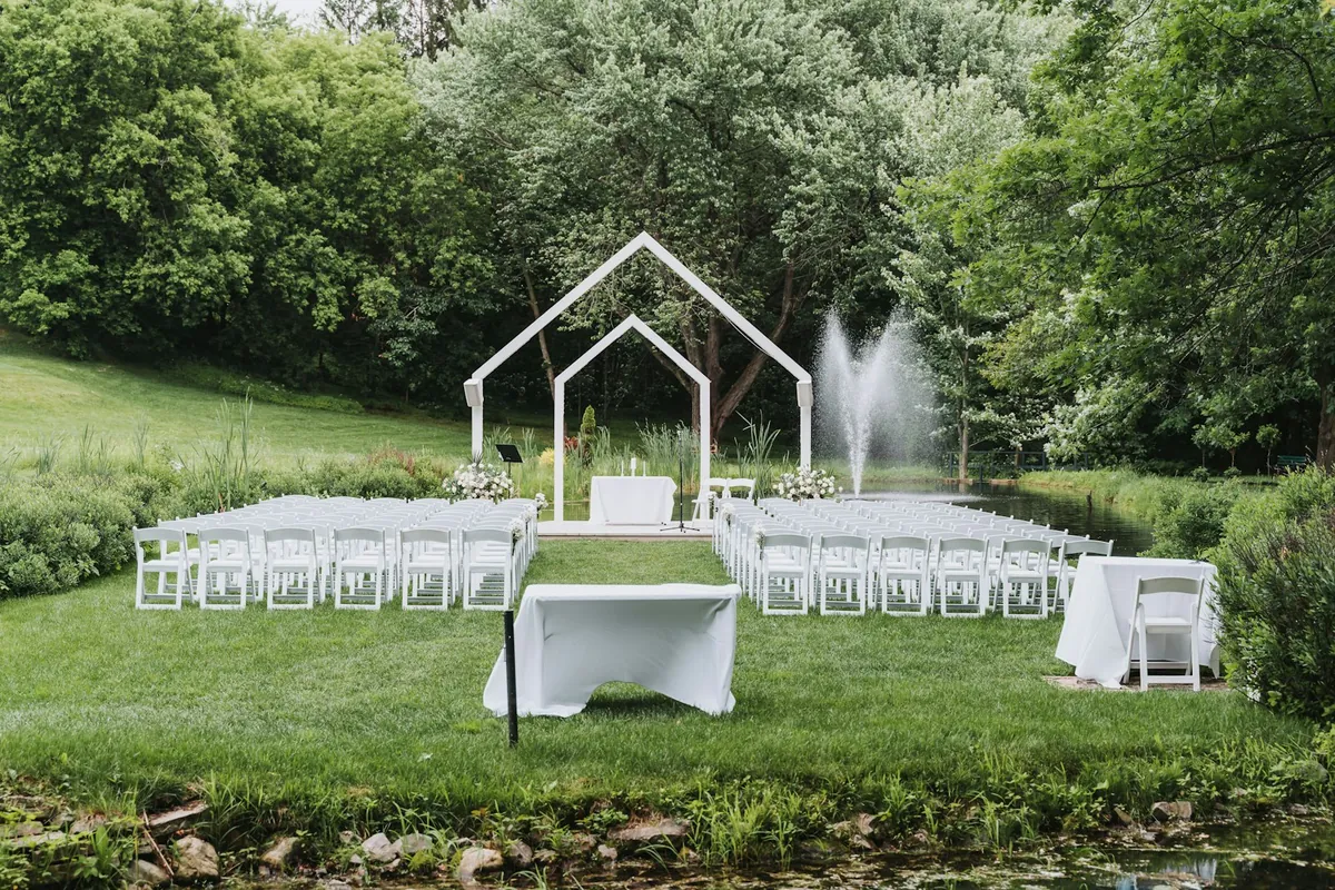 Rows of white ceremony chairs facing a decorated altar with trees and water in the background