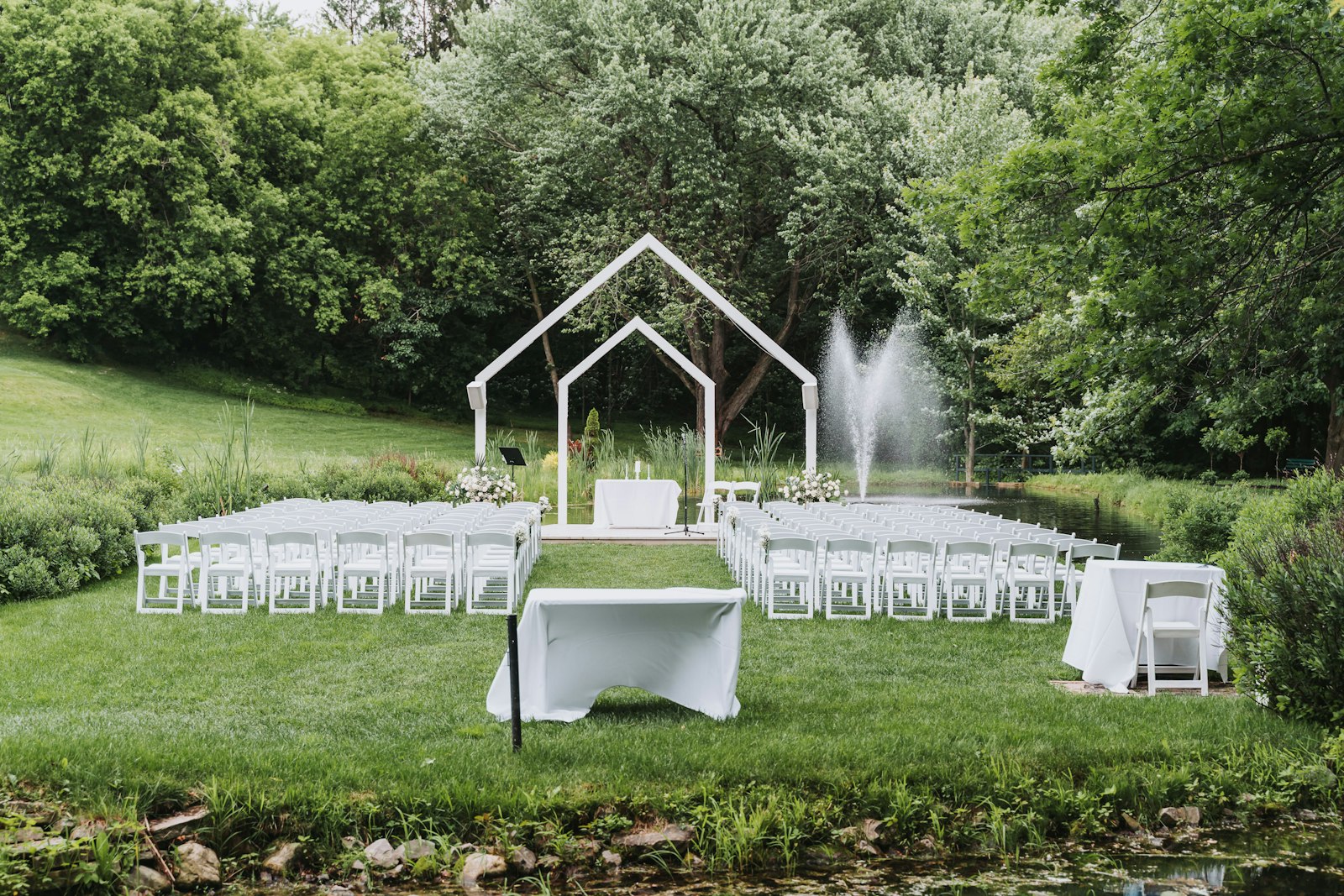 Rows of white ceremony chairs facing a decorated altar with trees and water in the background