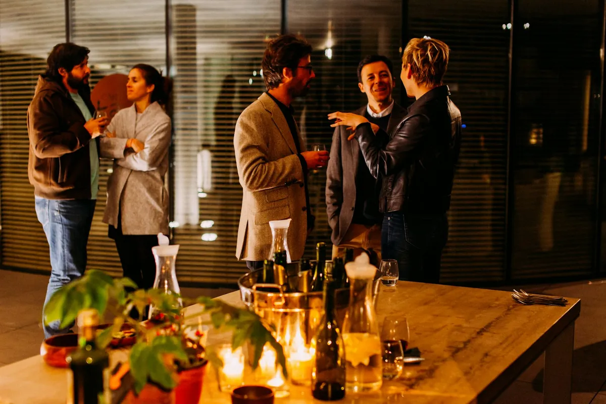 A row of cocktail-hour highboy tables at an outdoor reception with guests in conversation