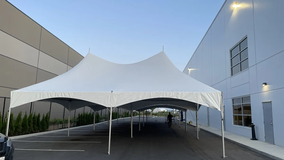 A long frame tent covering a parking lot between two commercial buildings at dusk