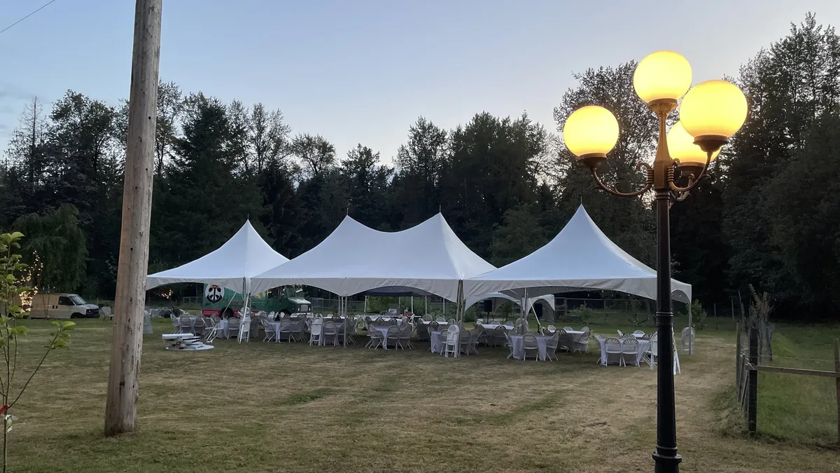 Three connected high-peak tents glowing at dusk on a rural property