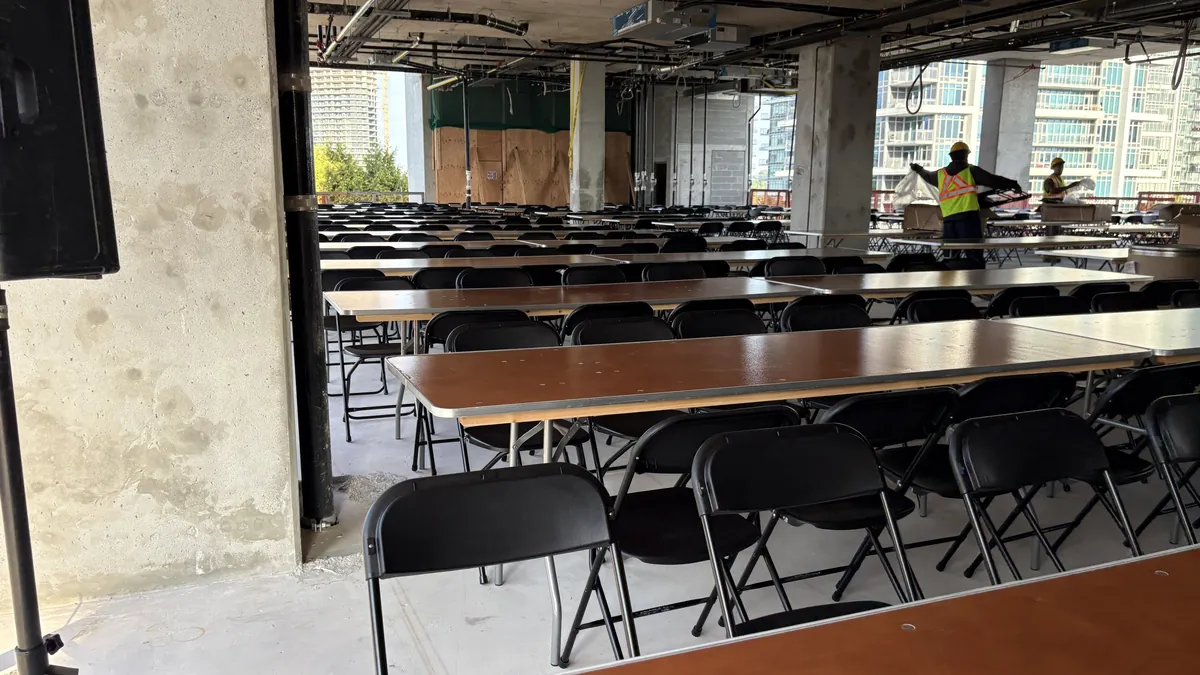 Rows of banquet tables and black folding chairs set up inside an unfinished building for a site event