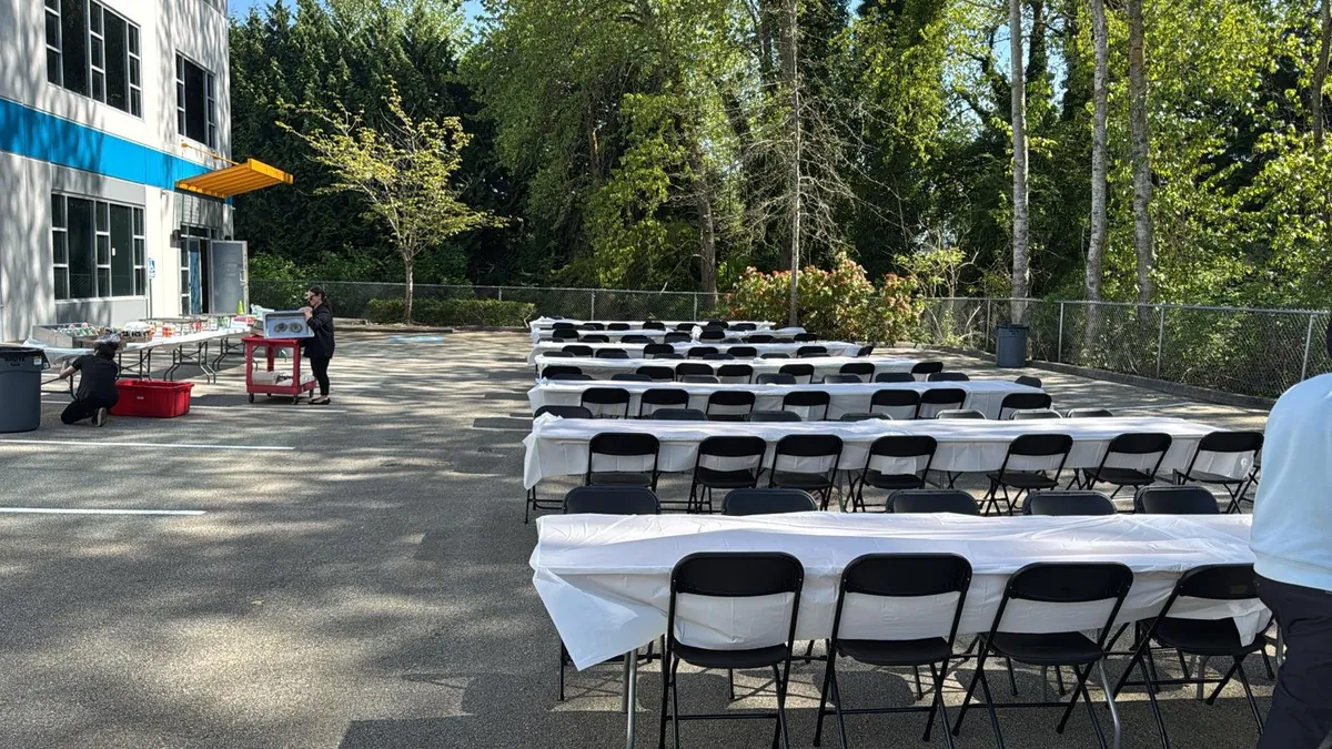 Banquet tables with white linens and black folding chairs set up outside an office building