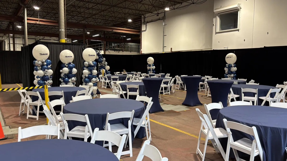Round tables in navy linens with white folding chairs and cocktail tables staged for a corporate party