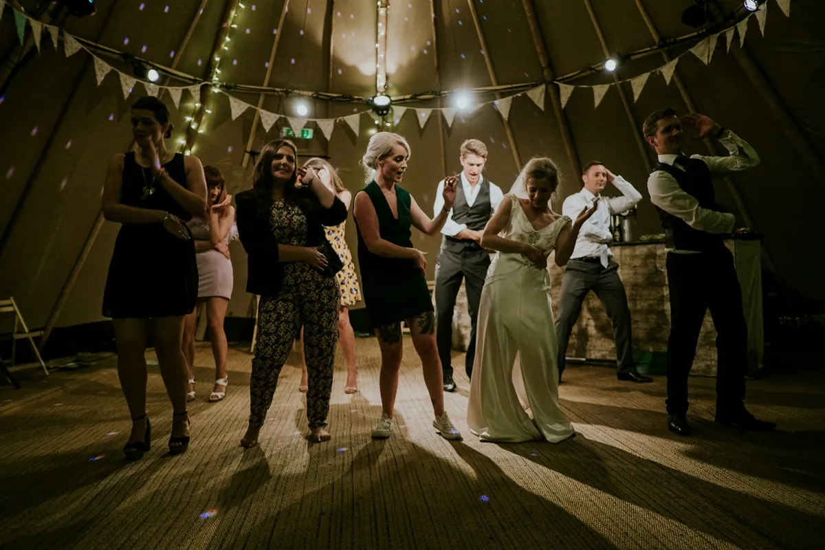 A wedding marquee with guests dancing at night under festive lighting