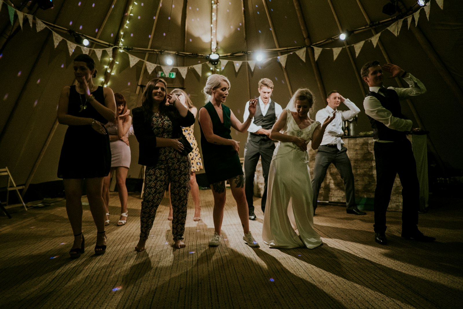 A wedding marquee with guests dancing at night under festive lighting