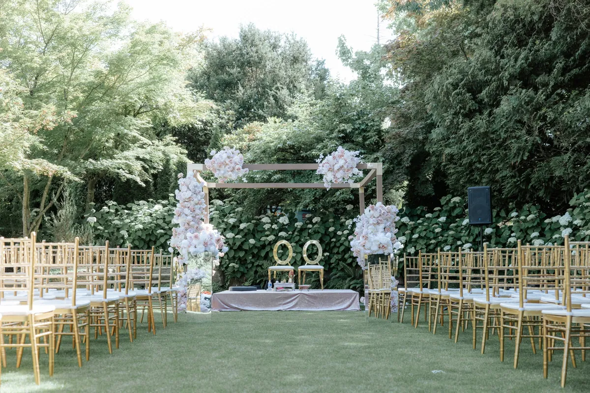 Rows of gold Chiavari chairs facing a floral ceremony arch at a garden wedding