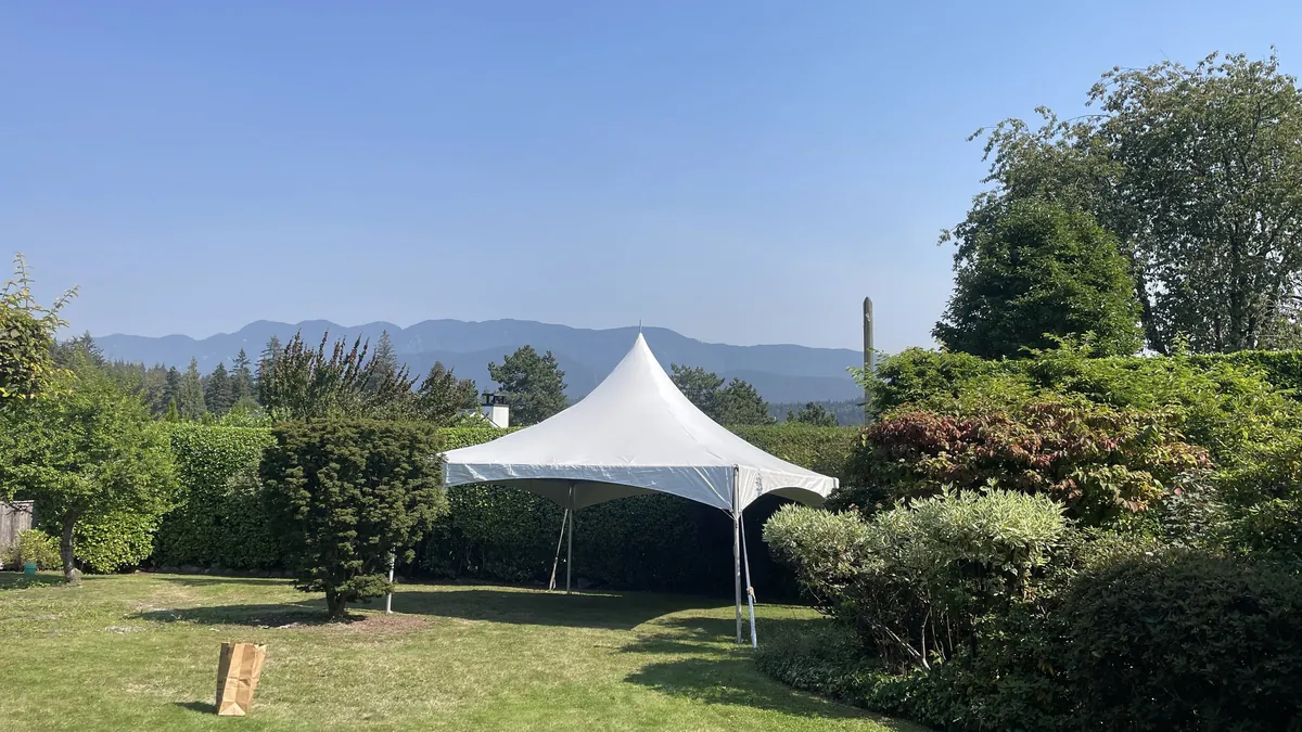 A high-peak frame tent on a manicured garden lawn with a mountain view behind