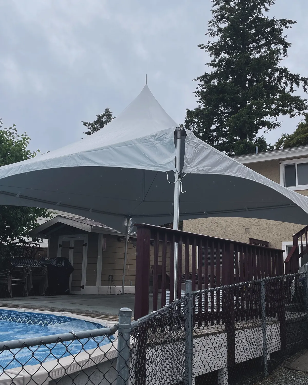 A high-peak frame tent shading a backyard pool deck