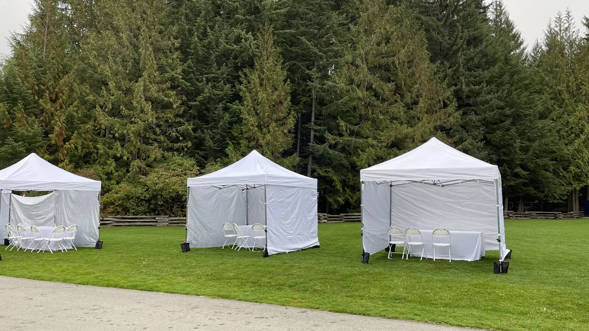 Three pop-up canopy tents with sidewalls and chairs set up on a grass field