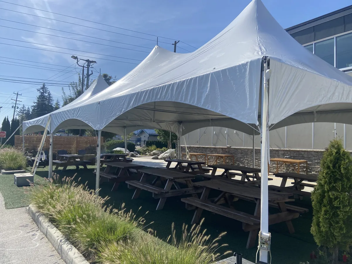 High-peak frame tents covering a restaurant patio lined with picnic tables