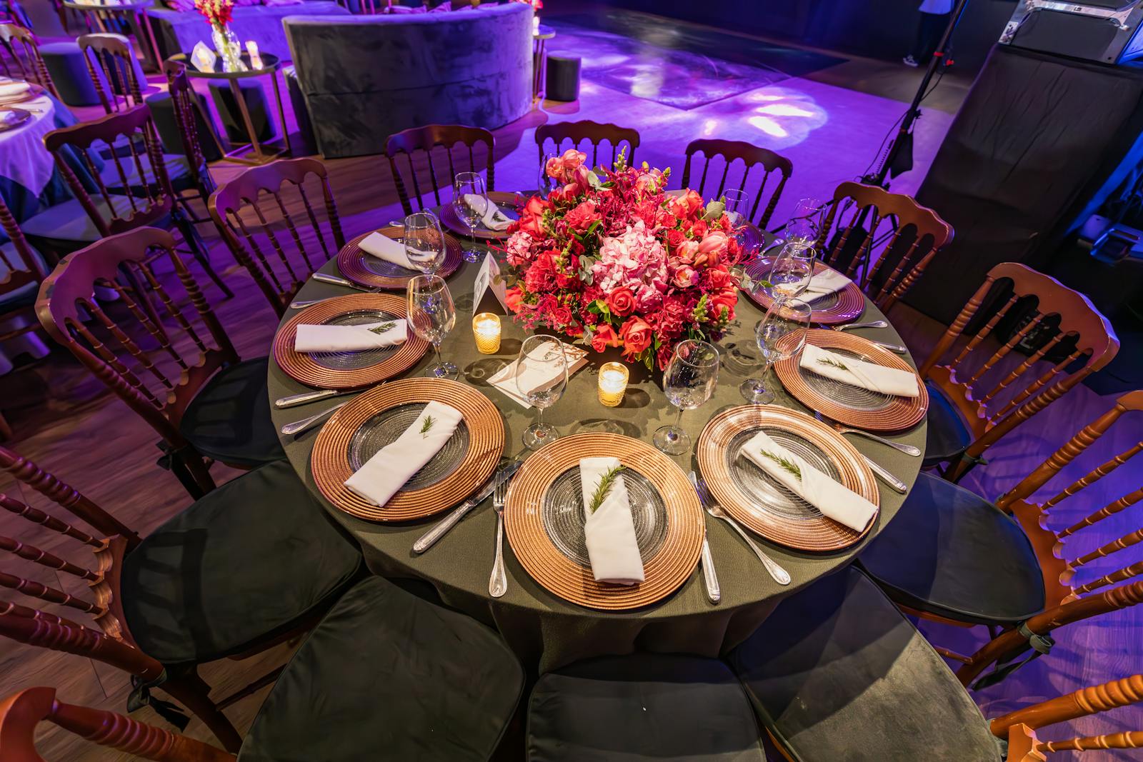 A formal round dinner table with full place settings, candles, and a floral centerpiece