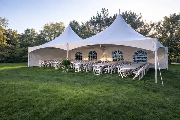 A long banquet table set up under a marquee at sunset with chairs and lighting