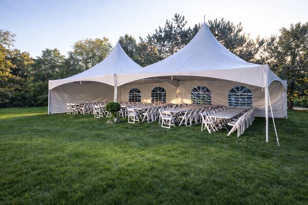 A wide white marquee tent set up at a backyard wedding with chairs and banquet tables underneath — the standard Delta reception footprint