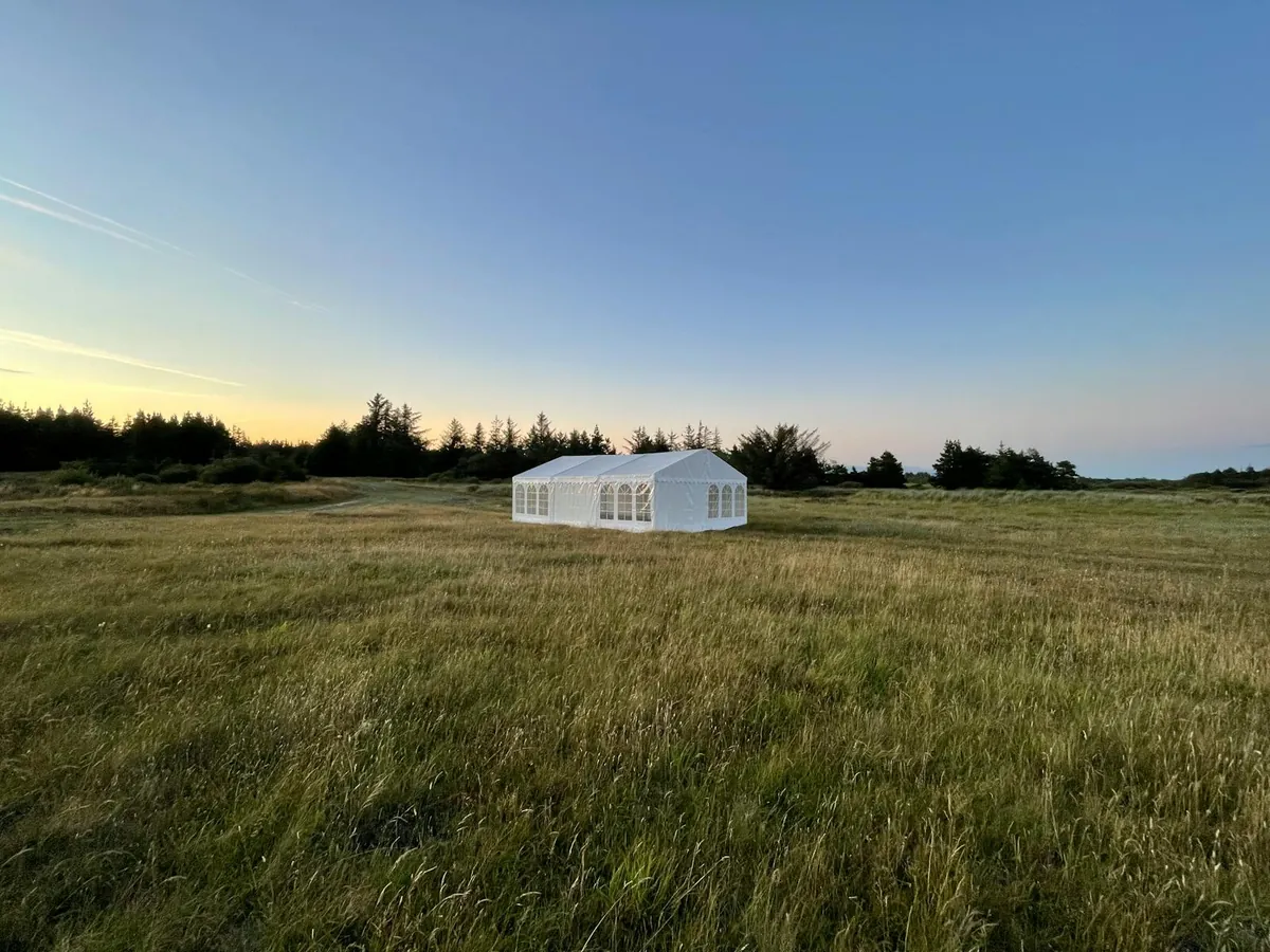 A clean white marquee tent standing alone in a vast open field — the standard 20×40 footprint