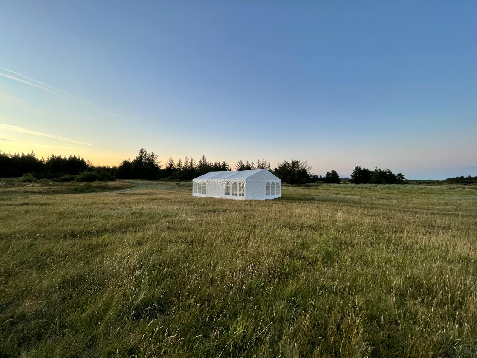 A clean white marquee tent standing alone in a vast open field at golden hour