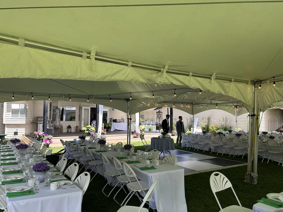 Banquet tables, fanback chairs, and a black-and-white checkered dance floor under a tent strung with bistro lights