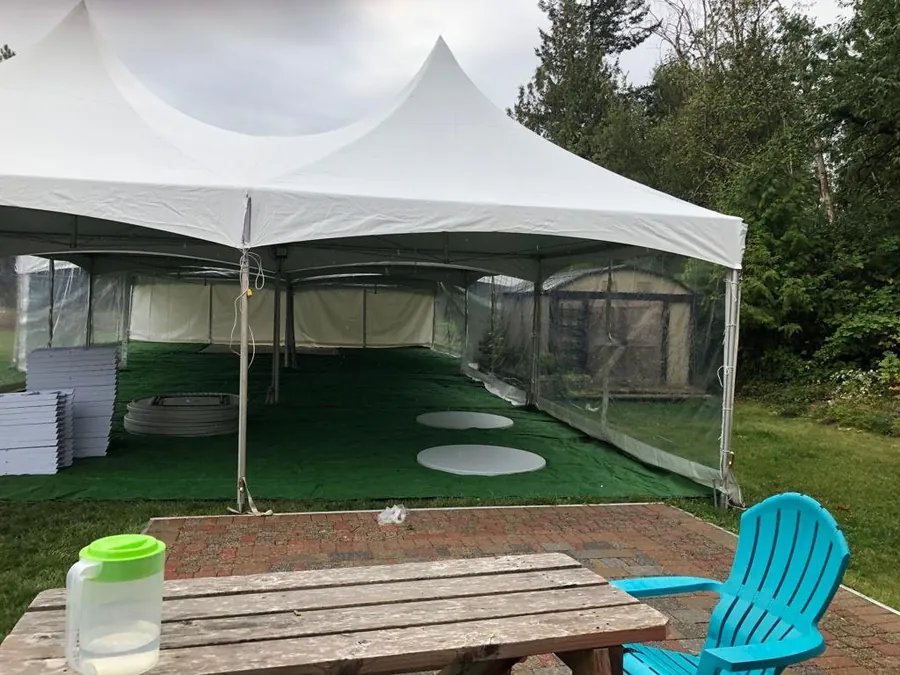 A frame tent mid-setup with turf flooring down and tables still stacked