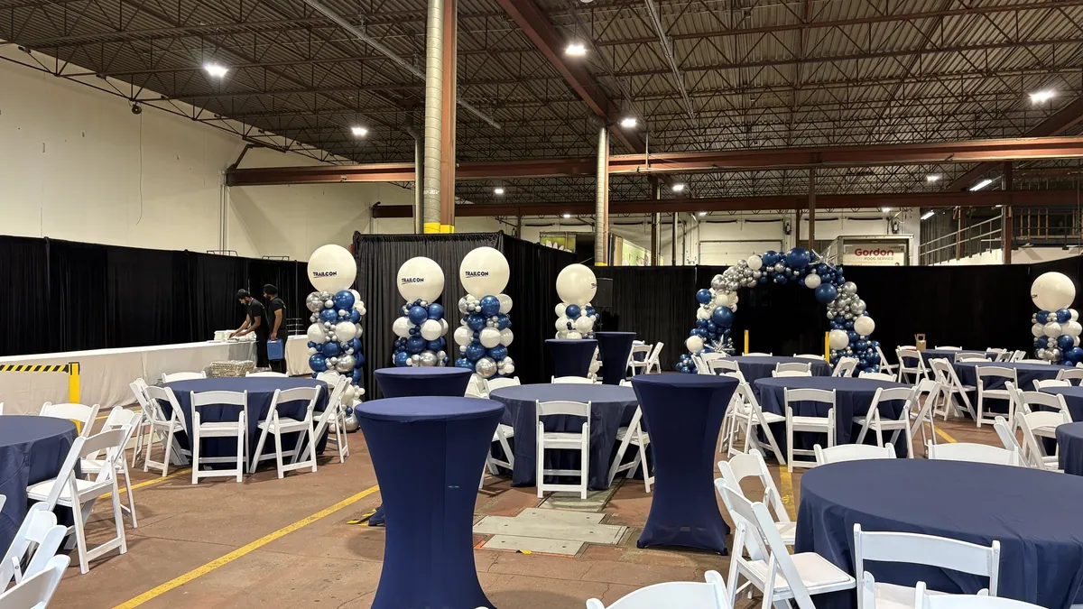 Round tables, cocktail tables, and a balloon arch set up for a party inside a warehouse